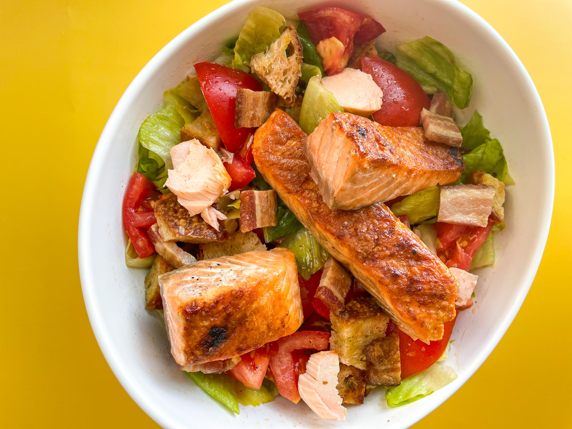 Grilled salmon BLT salad in white bowl.