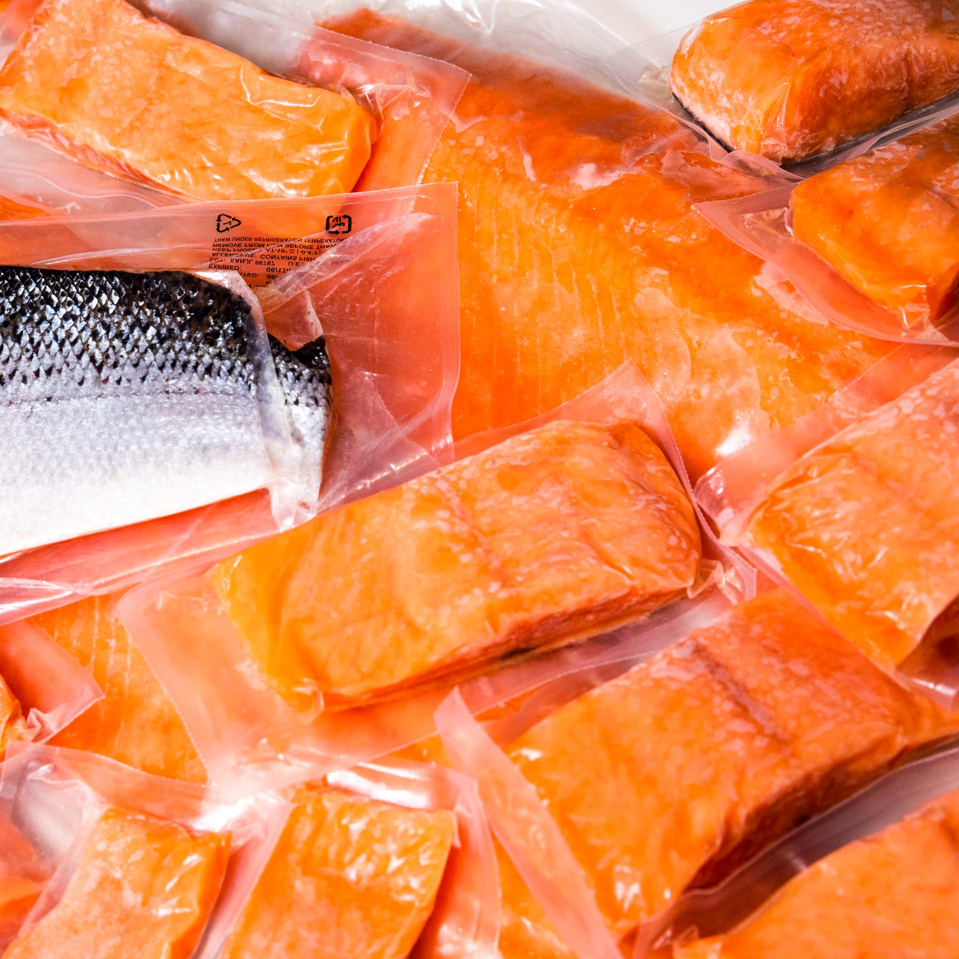 Pile of packaged salmon filets, one with skin side facing up.