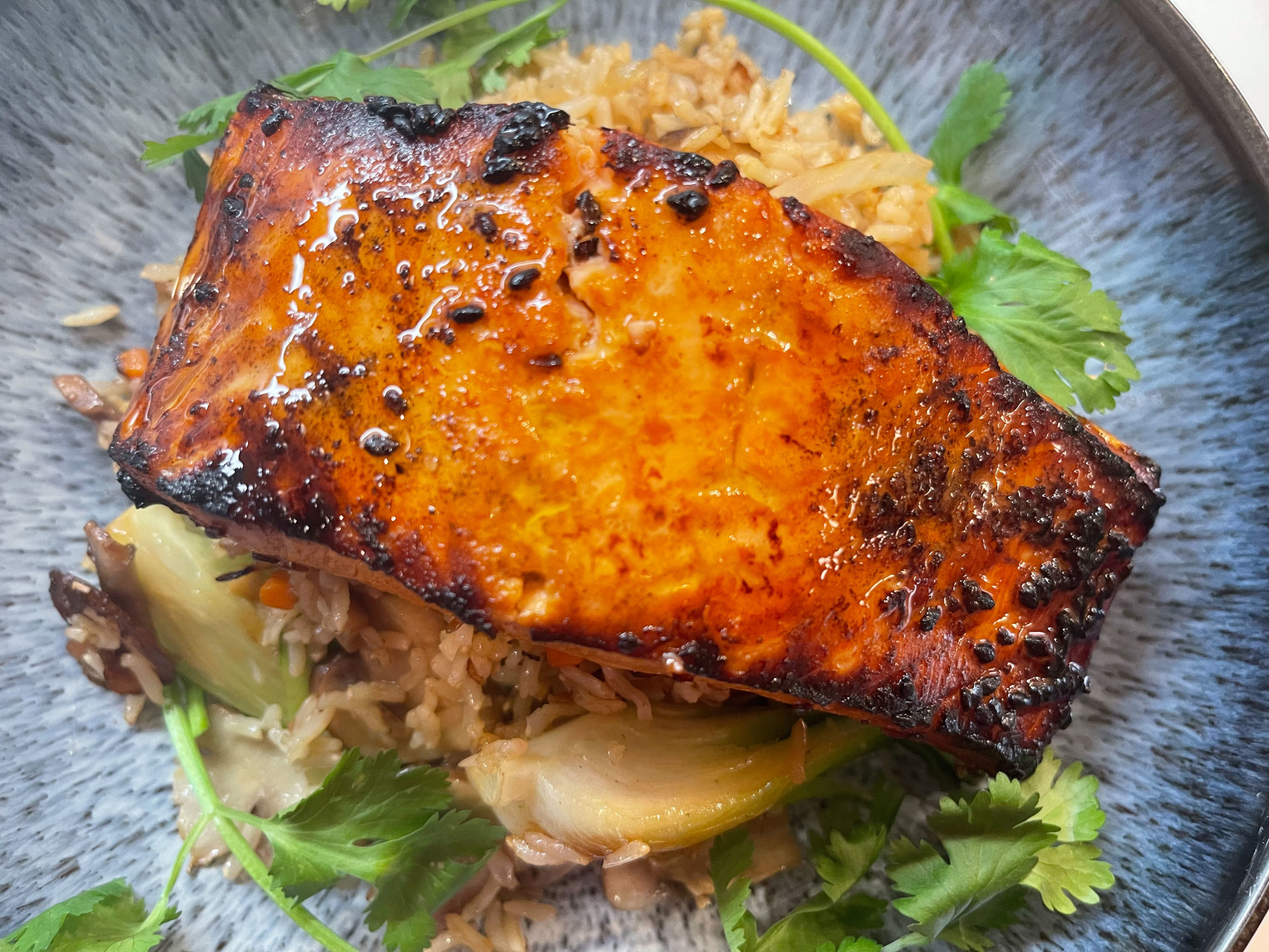 A fillet of Teriyaki Salmon sits on a bed of brown rice and veggies